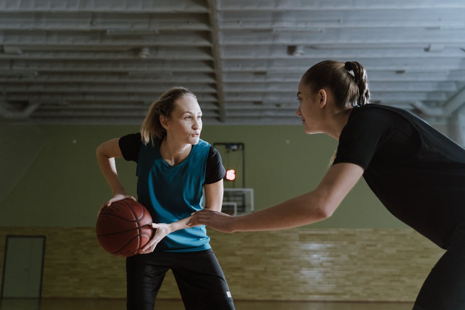 Two basketball players engaged in a one-on-one defense, showcasing athleticism and focus while a crowd cheers in the background.