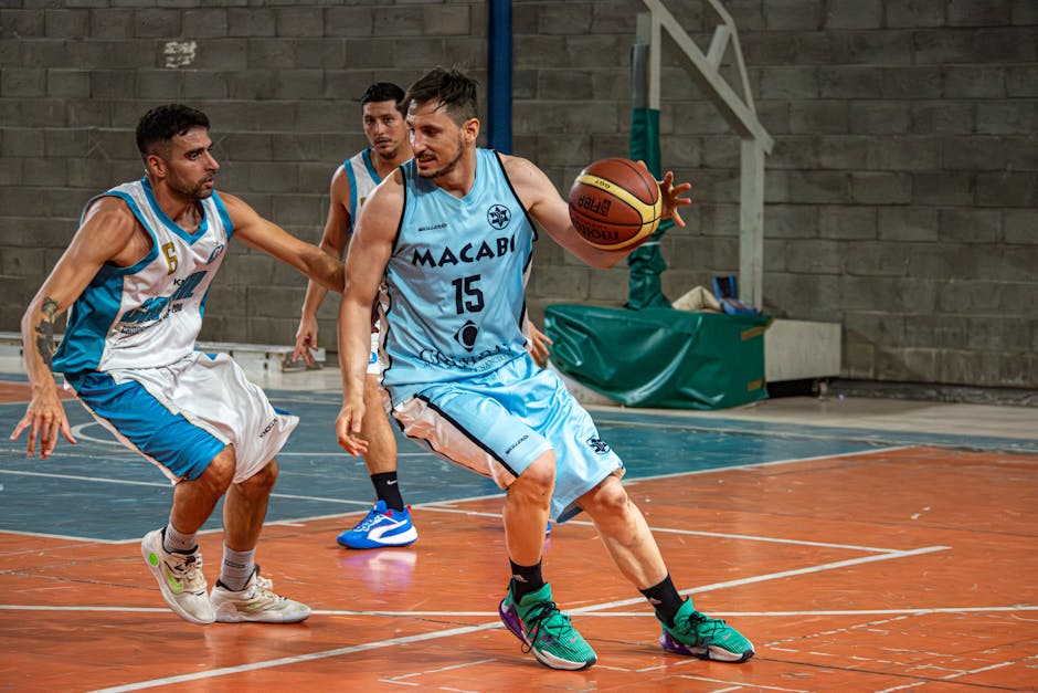 Basketball player in defensive stance on gym court with focus and intensity, blurred opponent in background